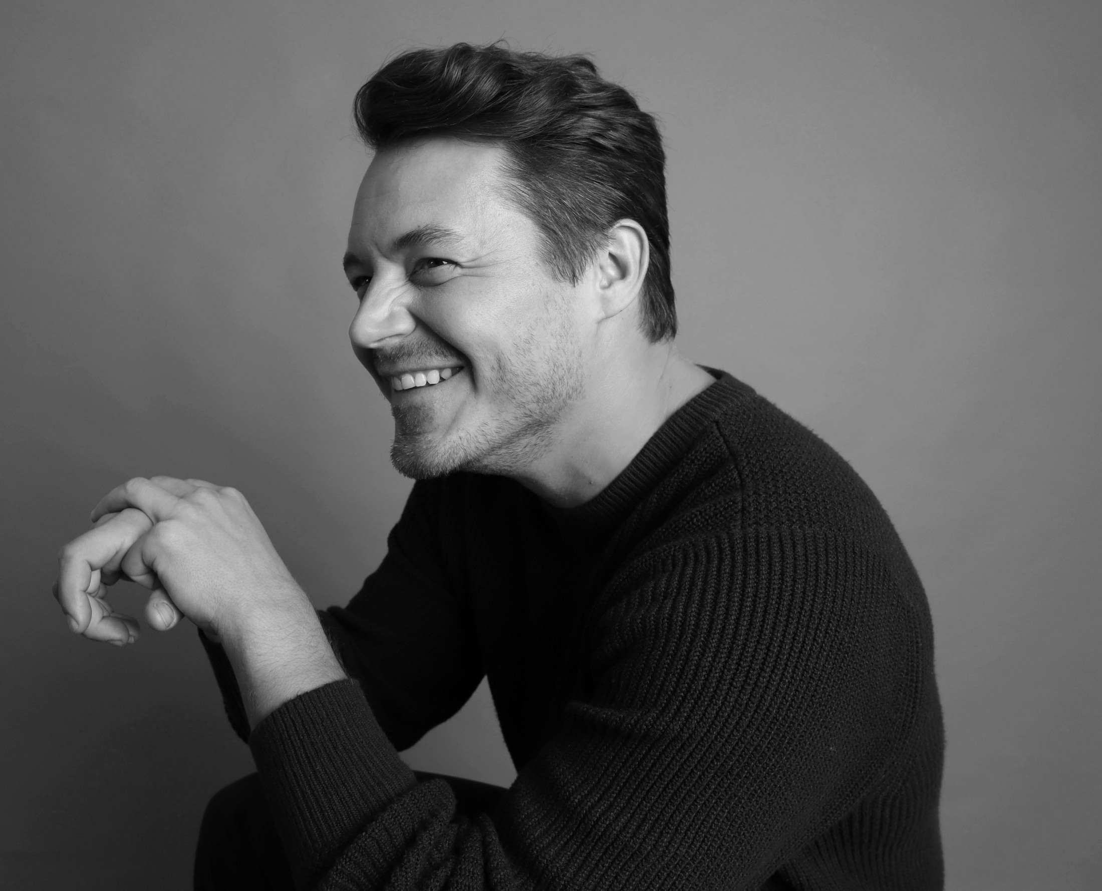 Bang Bang Stone, men's and masc groomer, smiling candidly in a black ribbed sweater