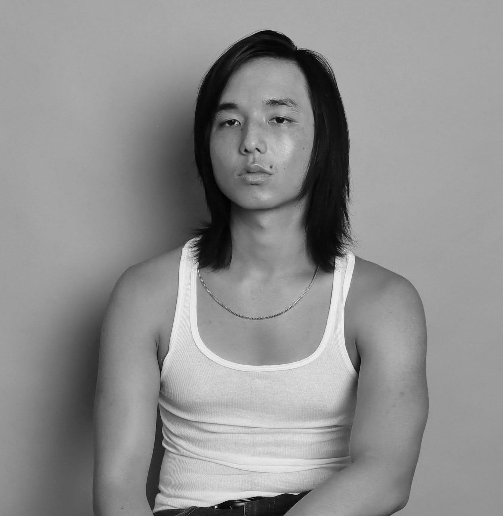 Black-and-white portrait of Ryan with sleek long hair and a fine chain necklace, Bang Bang Stone men's grooming