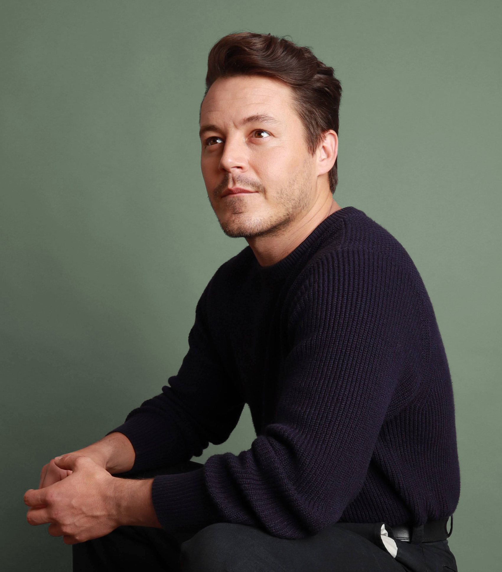 Seated three-quarter portrait in a navy ribbed sweater against a sage-green backdrop, Bang Bang Stone men's grooming