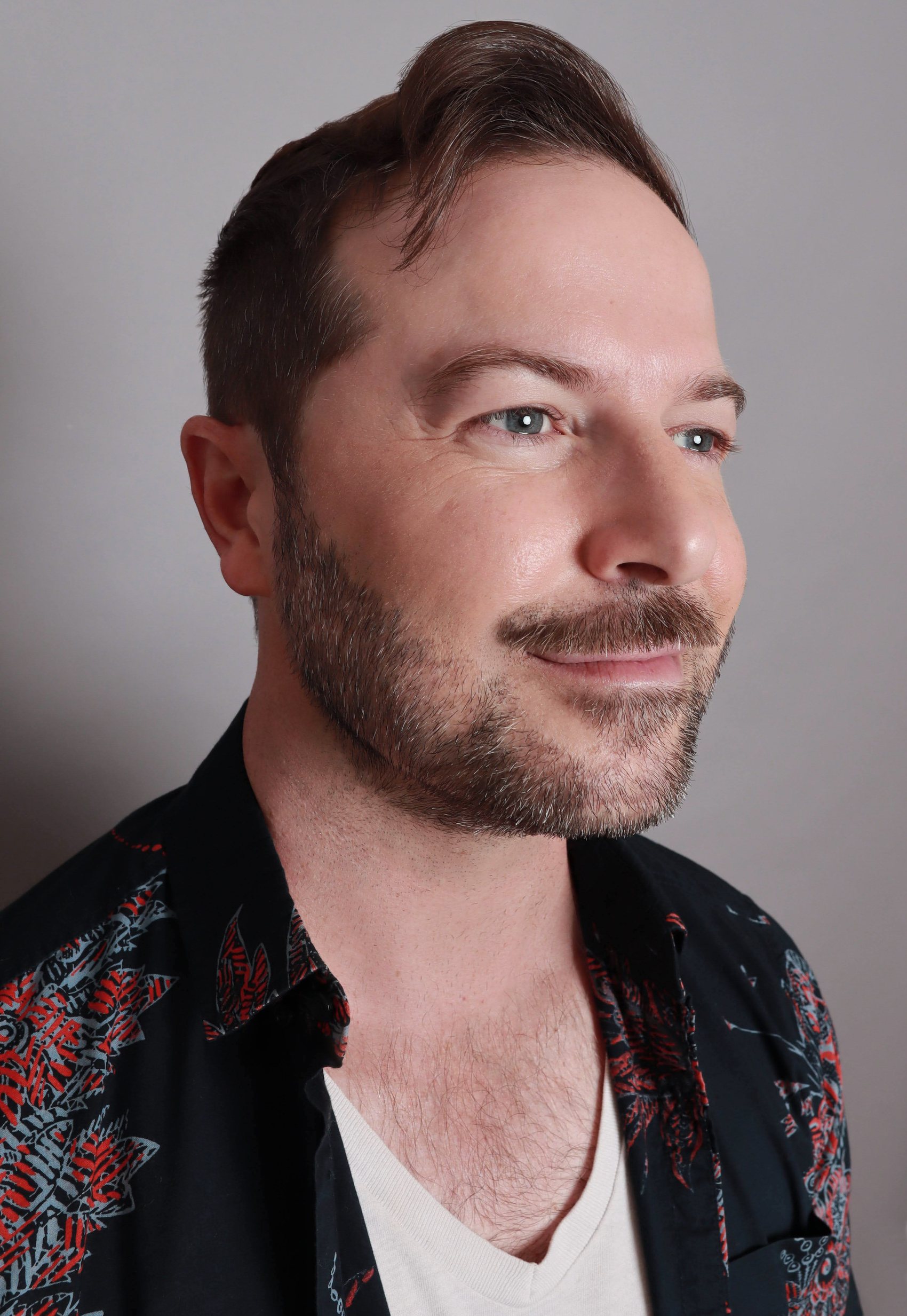 Three-quarter portrait in an open floral shirt over a white v-neck, soft side-swept hair, Bang Bang Stone men's grooming