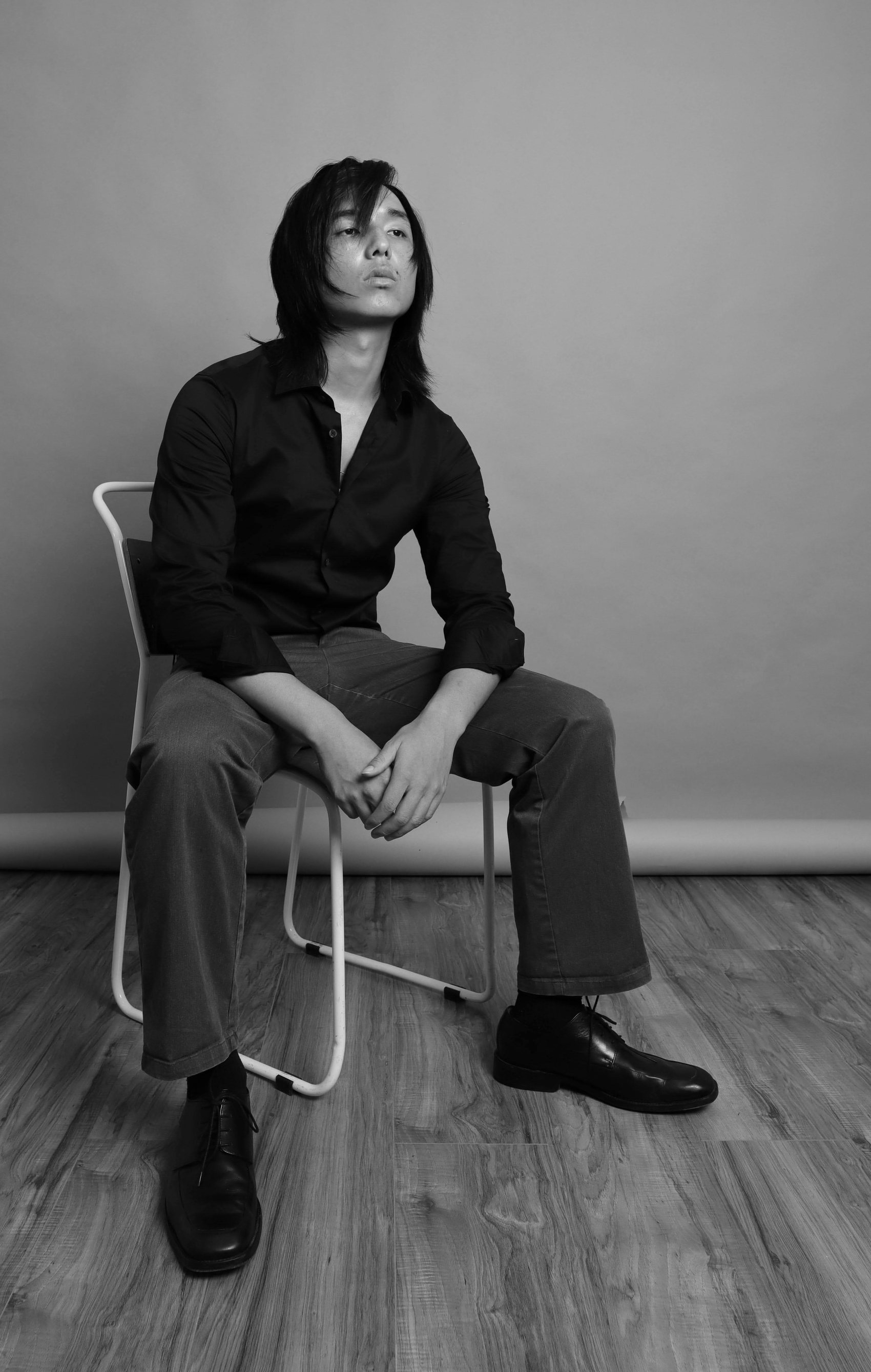 Black-and-white seated portrait of Ryan in a buttoned shirt with long hair, hands clasped, Bang Bang Stone grooming work