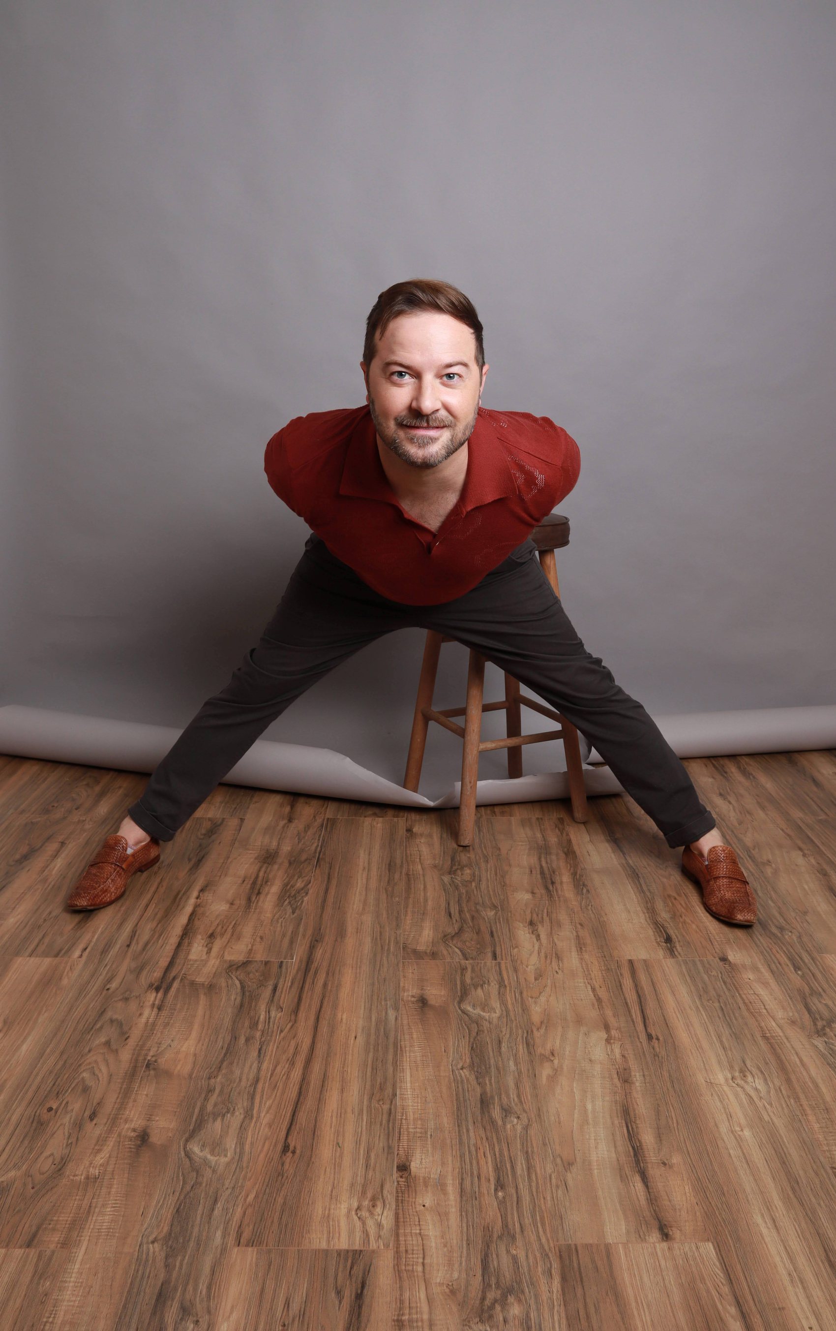 Playful wide-stance portrait in a red polo shirt on a wood floor, textured pompadour, Bang Bang Stone grooming work