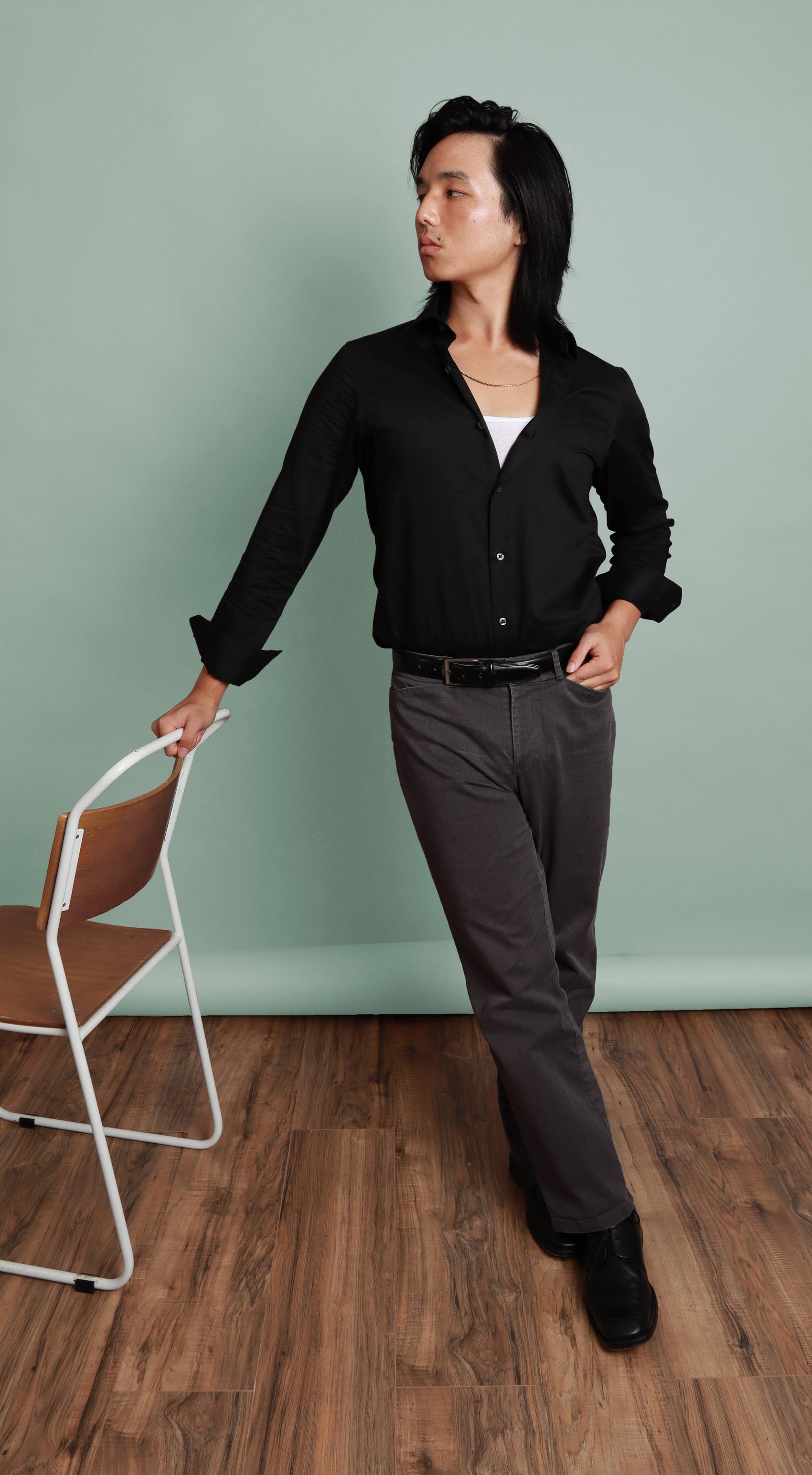 Portrait against a sage-green backdrop in an open black shirt over a white tank with a chain necklace, Bang Bang Stone men's grooming
