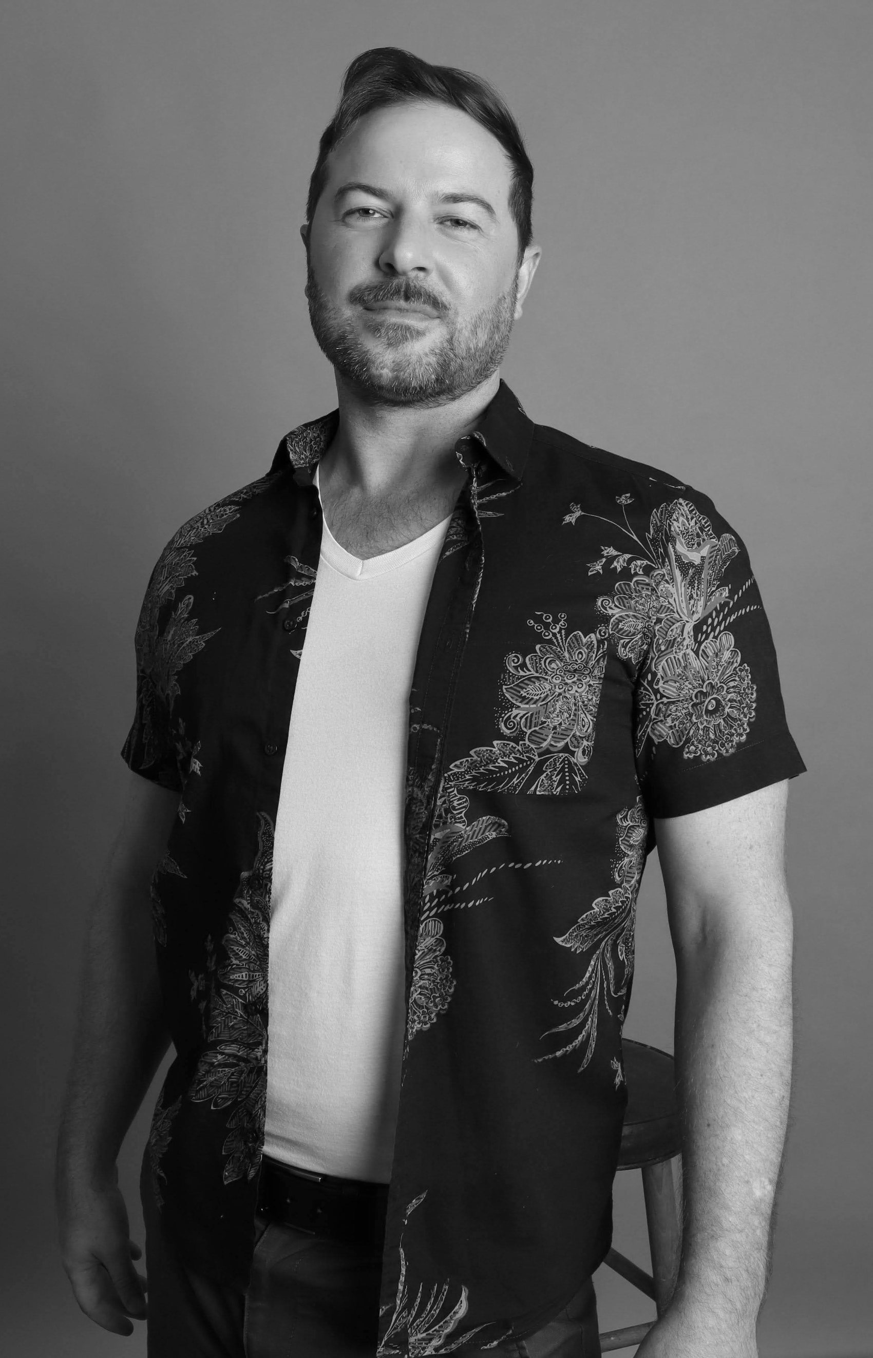 Black-and-white portrait in an open floral shirt over a white v-neck, swept-back hair, Bang Bang Stone grooming work